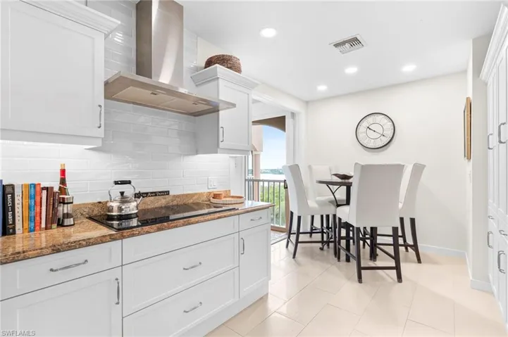 Kitchen featuring white cabinetry, tasteful backsplash, light stone counters, and wall chimney range hood