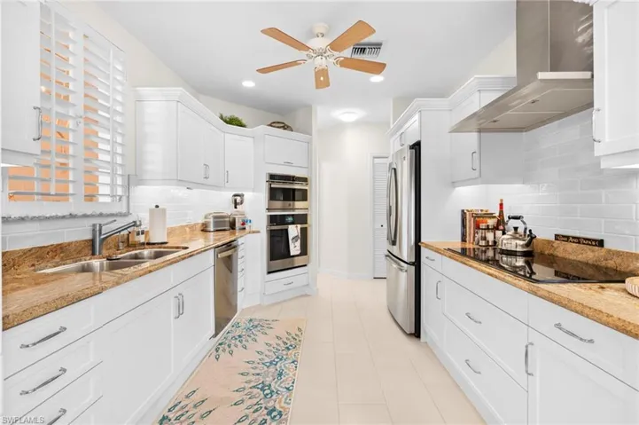 Kitchen with appliances with stainless steel finishes, sink, white cabinetry, ceiling fan, and wall chimney range hood