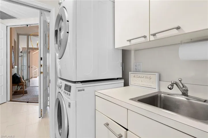 Laundry room featuring light tile patterned flooring, stacked washer and clothes dryer, cabinets, and sink