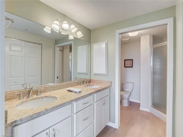 Bathroom featuring double vanity, a stall shower, and light wood-style flooring