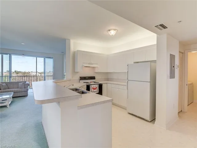 Kitchen featuring white appliances, light countertops, open floor plan, a peninsula, and white cabinetry