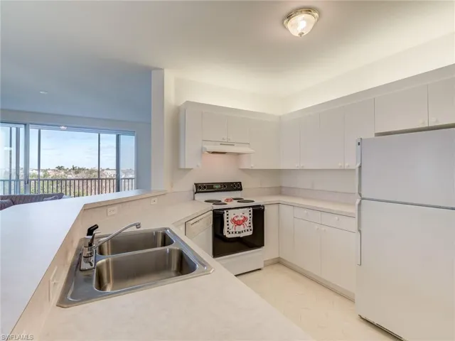 Kitchen featuring white appliances, light countertops, under cabinet range hood, white cabinetry, and a peninsula