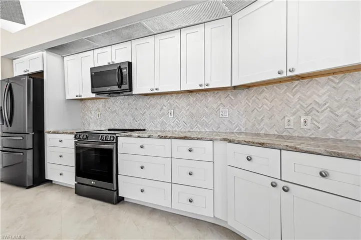 Kitchen featuring appliances with black stainless steel finishes, white cabinetry, light stone counters, and light tile backsplash