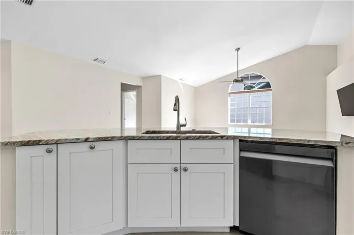 Kitchen island with light stone countertops, dishwashing machine, lofted ceiling, white cabinets, and a ceiling fan