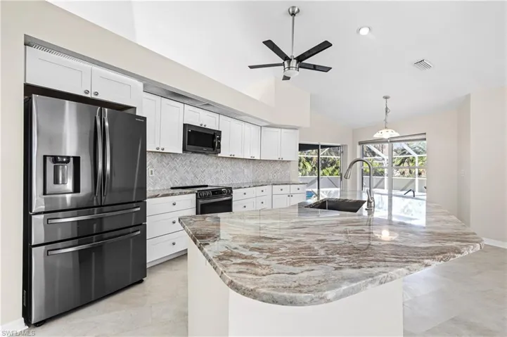 Kitchen with appliances with stainless steel finishes, light stone countertops, backsplash, white cabinetry, and a center island with sink