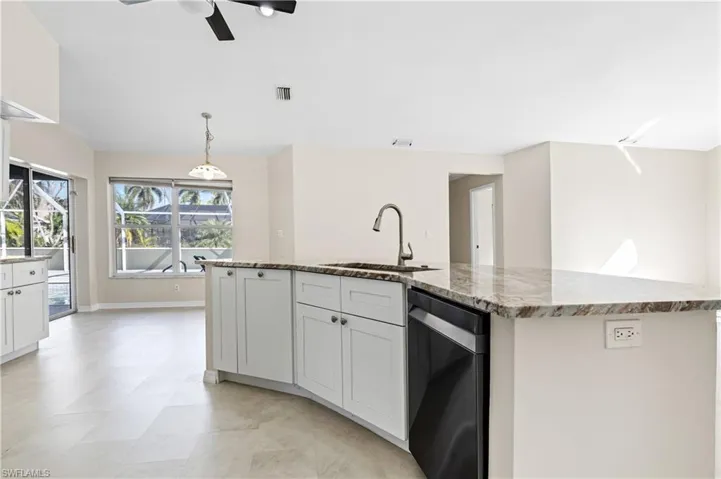 Kitchen with white cabinetry, light stone countertops, a kitchen island with sink, and black dishwasher