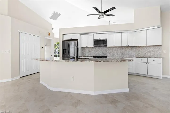 Kitchen with light stone countertops, white cabinets, tasteful backsplash, and high vaulted ceiling
