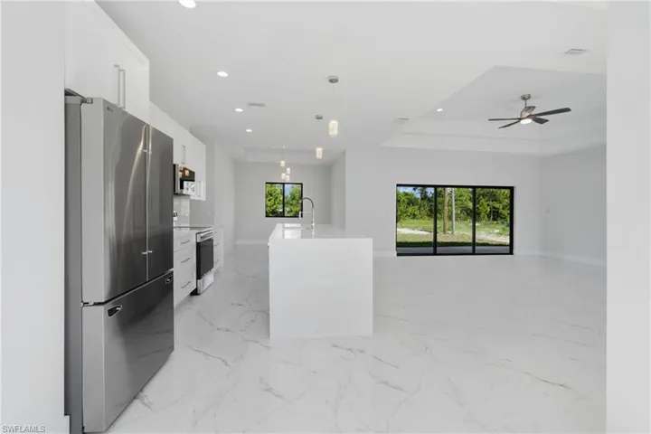 Kitchen with white cabinetry, light tile patterned floors, a kitchen island with sink, appliances with stainless steel finishes, and a raised ceiling