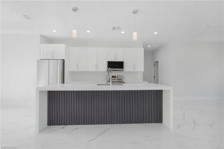 Kitchen featuring appliances with stainless steel finishes, decorative light fixtures, a large island, light tile patterned flooring, and white cabinetry