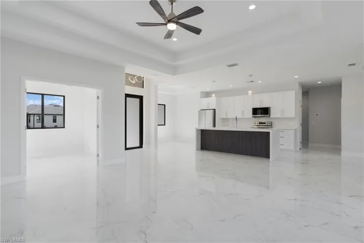 Unfurnished living room featuring sink, ceiling fan, a raised ceiling, and light tile patterned floors
