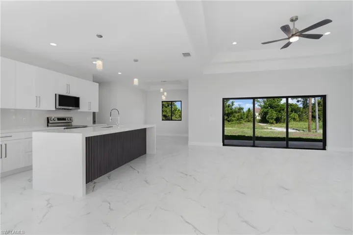 Kitchen featuring decorative light fixtures, light tile patterned flooring, stainless steel appliances, a center island with sink, and a raised ceiling