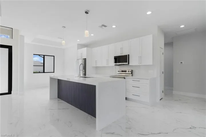 Kitchen featuring white cabinets, light tile patterned floors, sink, and an island with sink