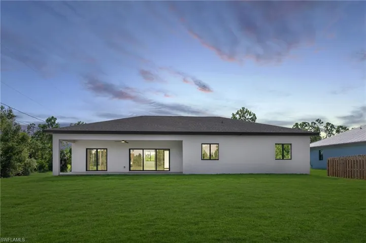 Back house at dusk featuring a lawn