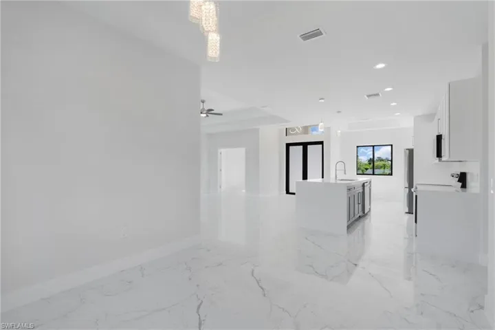 Empty room with light tile patterned floors, ceiling fan with notable chandelier, and sink