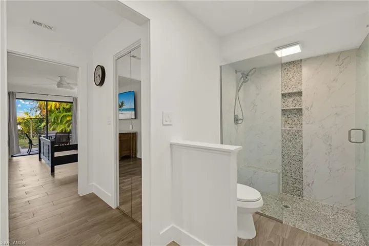 Bathroom with tiled shower, hardwood / wood-style floors, ceiling fan, and toilet