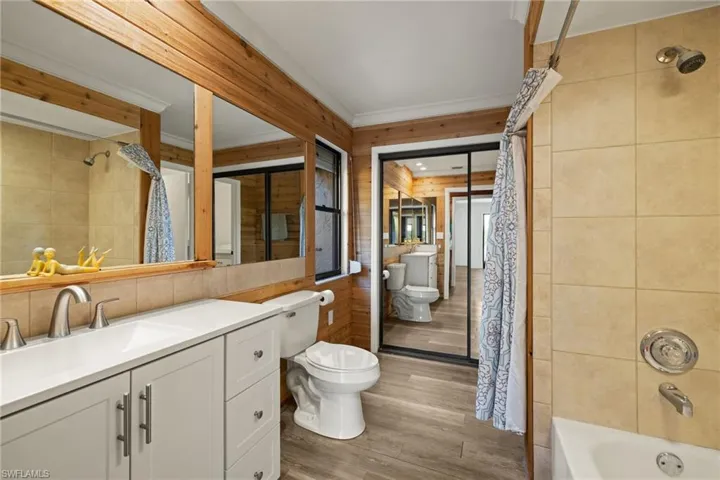 Full bathroom featuring hardwood / wood-style flooring, tile walls, vanity, shower / bath combination with curtain, and toilet