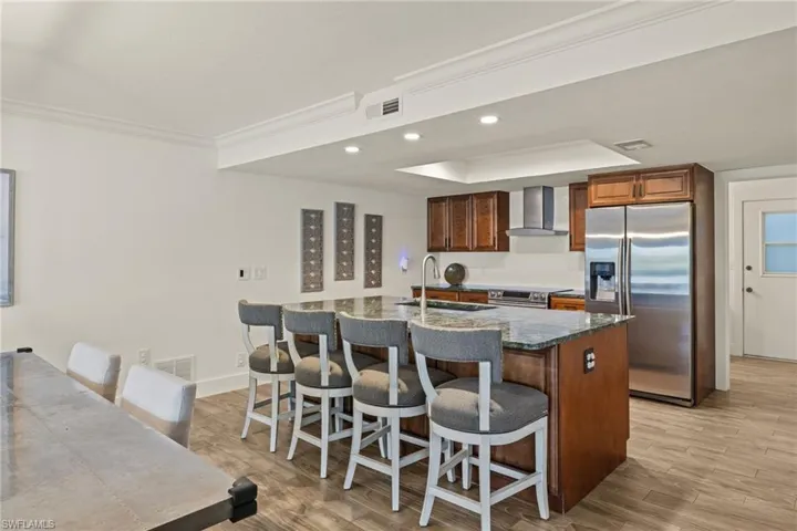 Kitchen with sink, wall chimney range hood, a kitchen island with sink, stainless steel appliances, and a kitchen breakfast bar