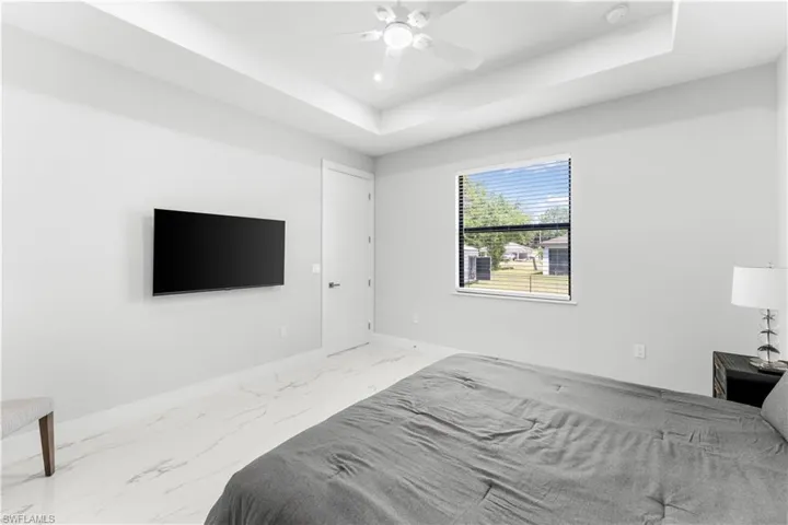 Spacious room featuring tray ceilings, a ceiling fan with integrated lighting, and white marble-look flooring
