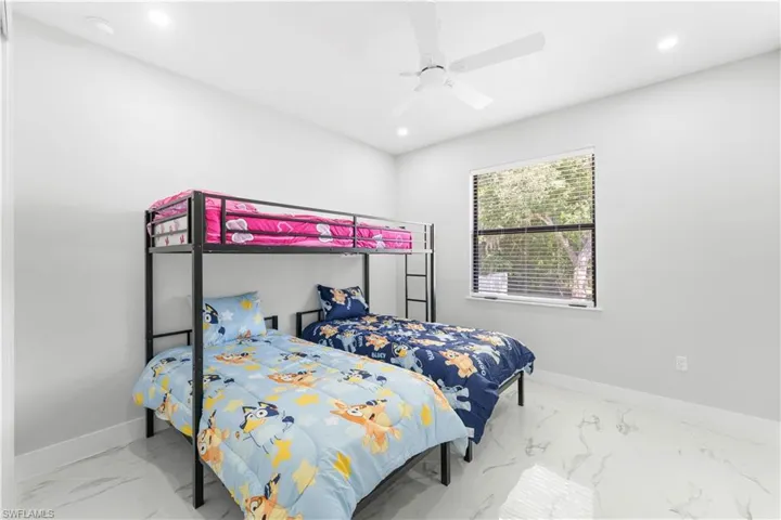 Bright room featuring large window with horizontal blinds, overhead ceiling fan, recessed lighting, and white baseboards with polished tile flooring