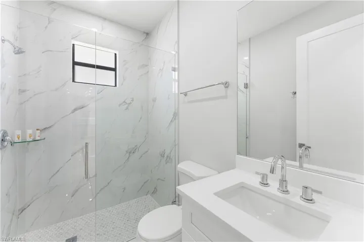 Modern bathroom featuring a glass-enclosed shower with large format tile walls and a mosaic tile floor, a window with black trim, a vanity with an integrated sink and chrome fixtures, and a frameless mirror
