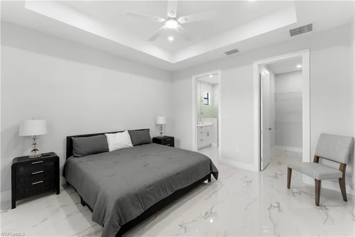 Spacious bedroom featuring large format tile flooring, a tray ceiling with recessed lighting, and a ceiling fan