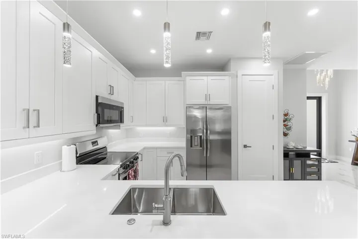 Modern kitchen featuring white shaker cabinetry, stainless steel appliances, a double basin stainless steel sink, quartz countertops, and recessed lighting with decorative pendant fixtures