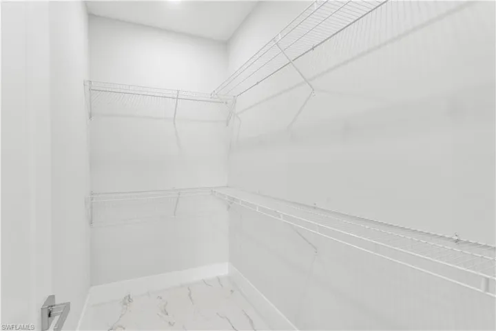 Walk-in closet featuring white wire shelving on multiple walls, a light fixture, and marble-look floor tiles