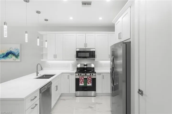 Modern kitchen with white shaker cabinetry, stainless steel appliances, white countertops, and contemporary pendant lighting fixtures