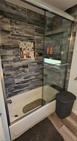 Full bathroom with enclosed tub / shower combo and wood finished floors