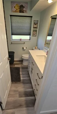 Half bath with toilet, baseboards, wood finished floors, and vanity