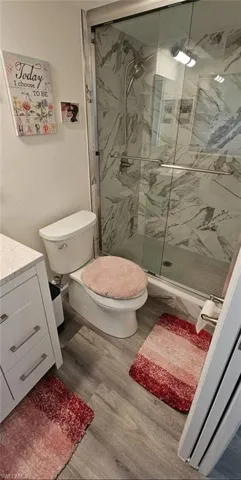 Bathroom featuring a marble finish shower, vanity, toilet, and wood finished floors