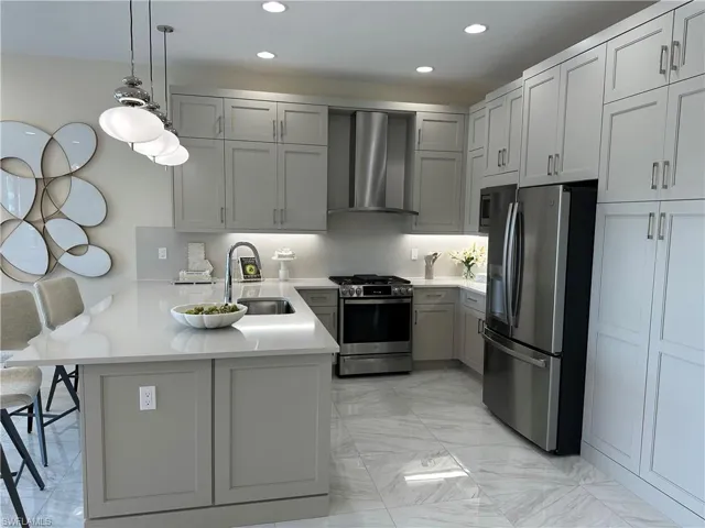 Kitchen featuring stainless steel appliances, gray cabinets, light countertops, wall chimney range hood, and a peninsula