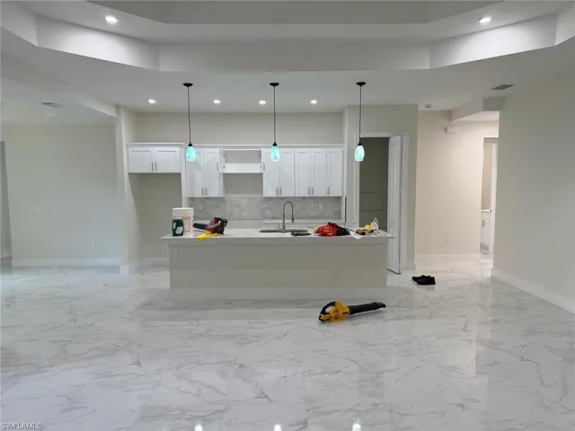 Kitchen with recessed lighting, white cabinetry, tasteful backsplash, a kitchen island with sink, and pendant lighting