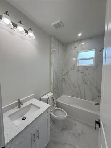 Bathroom with vanity, washtub / shower combination, and marble look tiles