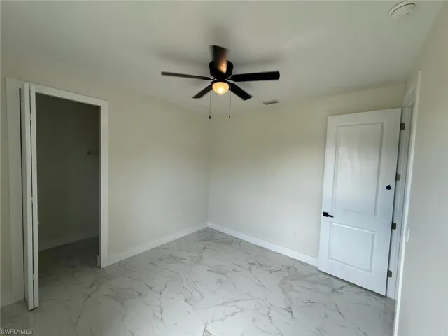 Unfurnished bedroom featuring light marble finish floors and a ceiling fan