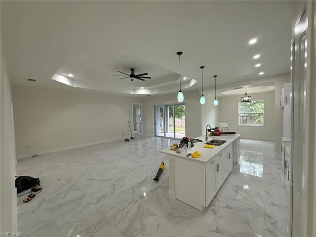 Kitchen featuring recessed lighting, a tray ceiling, open floor plan, white cabinets, and a kitchen island with sink