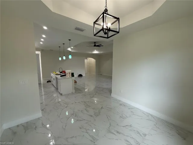 Unfurnished dining area with arched walkways, ceiling fan, light marble finish floors, a chandelier, and a raised ceiling