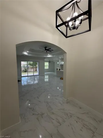 Hallway with arched walkways, a tray ceiling, and marble finish flooring