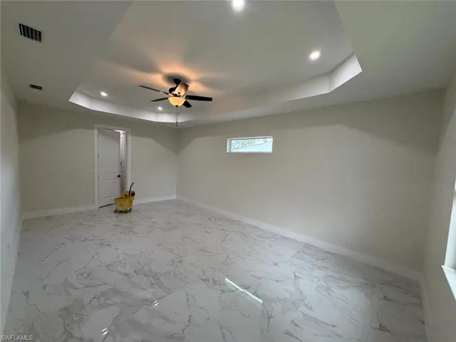Unfurnished room with a raised ceiling, ceiling fan, recessed lighting, and marble finish flooring