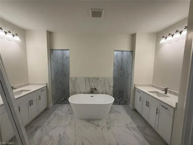 Full bath with two vanities, marble finish flooring, a freestanding tub, wainscoting, and tile walls