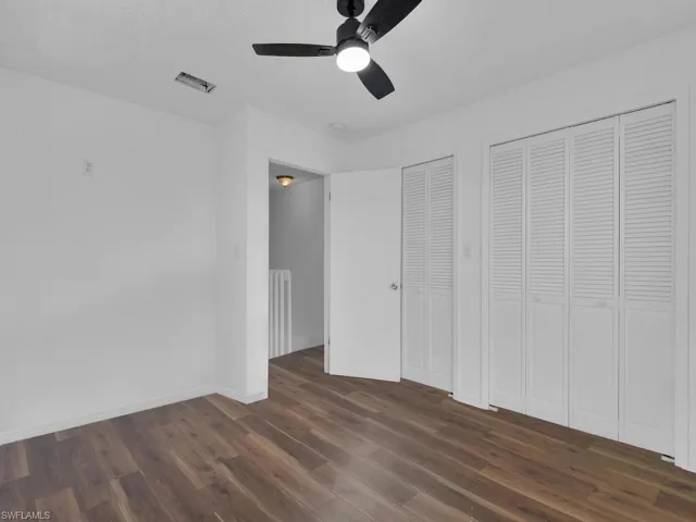 Unfurnished bedroom with dark wood-style floors, multiple closets, ceiling fan, and radiator heating unit