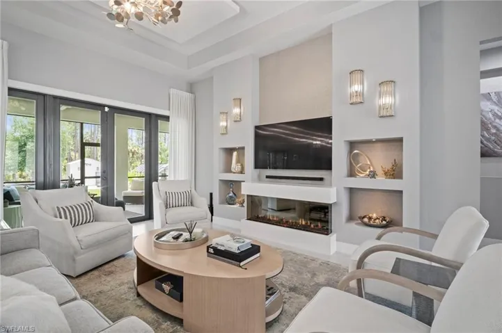 Living room with built in features, a glass covered fireplace, a chandelier, a towering ceiling, and french doors