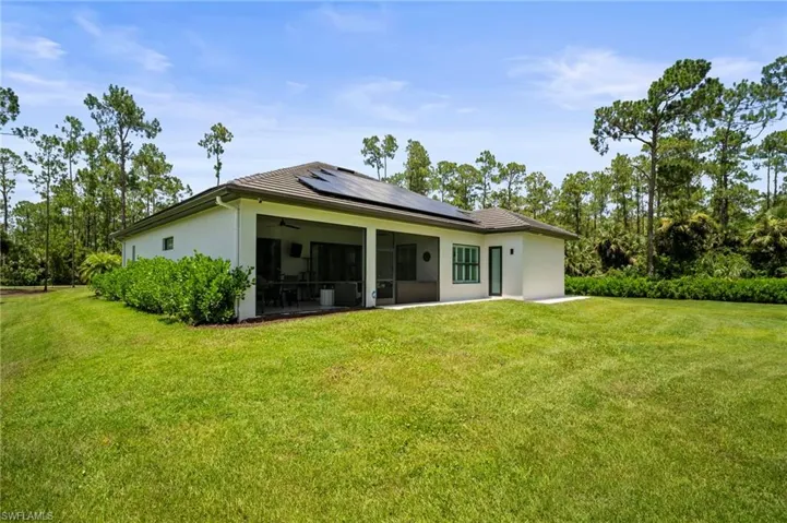 Back of property featuring solar panels, a sunroom, a lawn, and stucco siding