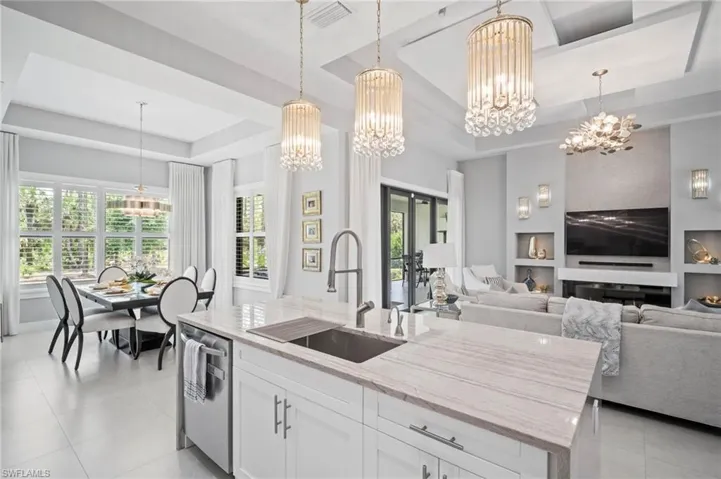 Kitchen featuring a raised ceiling, a chandelier, light stone counters, light tile patterned floors, and white cabinets