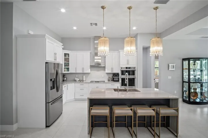 Kitchen featuring appliances with stainless steel finishes, tasteful backsplash, a chandelier, white cabinetry, and light stone counters