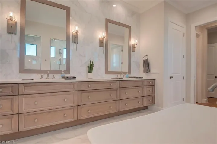 Bathroom with a freestanding tub, light marble finish flooring, and double vanity