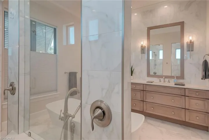 Bathroom featuring light marble finish floors, a stall shower, a soaking tub, and vanity