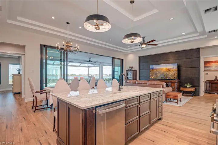 Kitchen with ceiling fan, light stone countertops, stainless steel dishwasher, a center island with sink, and hanging light fixtures
