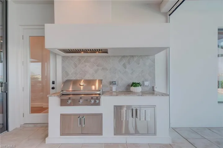 Kitchen with exhaust hood, light stone counters, light tile patterned floors, decorative backsplash, and white cabinetry