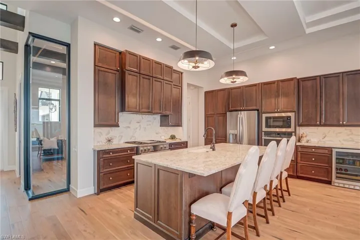Kitchen with decorative light fixtures, wine cooler, a breakfast bar area, appliances with stainless steel finishes, and light wood-style flooring